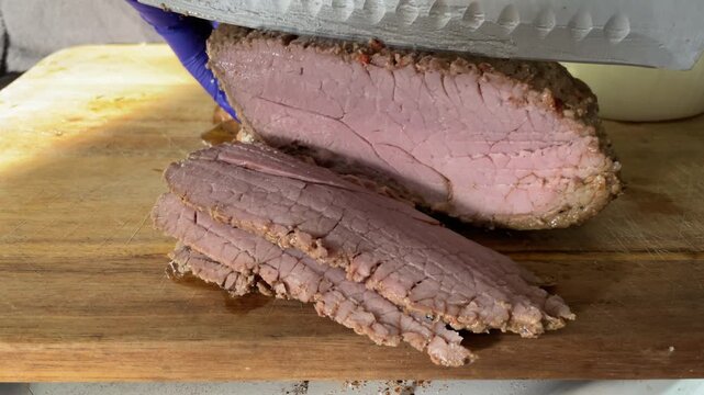 Close-up shot of chef hands using a sharp knife to slice a perfectly seared and roasted beef tri-tip steak on a wooden cutting board. The video captures the knife cutting smoothly against the grain.