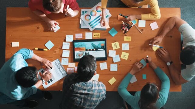 Top view of business people working together to design web design. Aerial view of designer brainstorming and discussing about website interface and looking at tablet with digital design. Symposium.