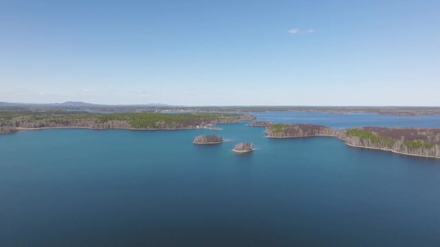 High angle panoramic footage over a wide blue freshwater lake dotted with scenic green forested islands and quiet shores under a clear bright sky on a sunny summer day