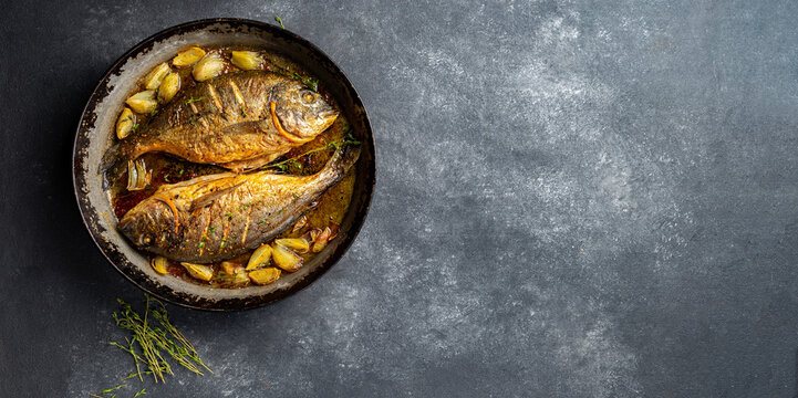 Baked sea bream or dorada with onion and herbs in pan on dark background