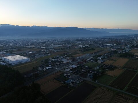 A broad checkerboard of cultivated plots and low buildings fades toward a mountain range in fading soft light.