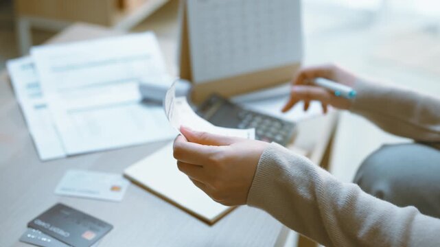 Receipt checking with a calculator illustrates finance and accounting as hands hold a narrow paper slip, press buttons and review budget documents for a careful personal finance calculation at home.
