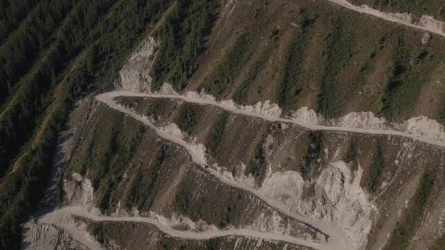 High angle view of vehicle traveling on scenic serpentine dirt road at Katu-Yaryk pass in Altai Republic, Russia, surrounded by steep rocky canyon slopes and wild mountain landscape