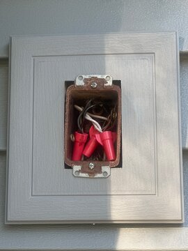 Open rusty outdoor electrical junction box with wires and red wire nuts in a vinyl siding mounting block