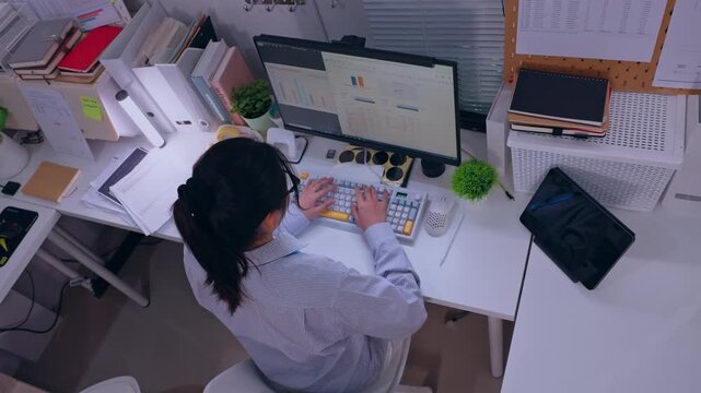 Overhead View of Woman Office Worker Typing on Computer Keyboard at Desk, Focused on Digital Work in Busy Workplace with Paperwork and Office Supplies