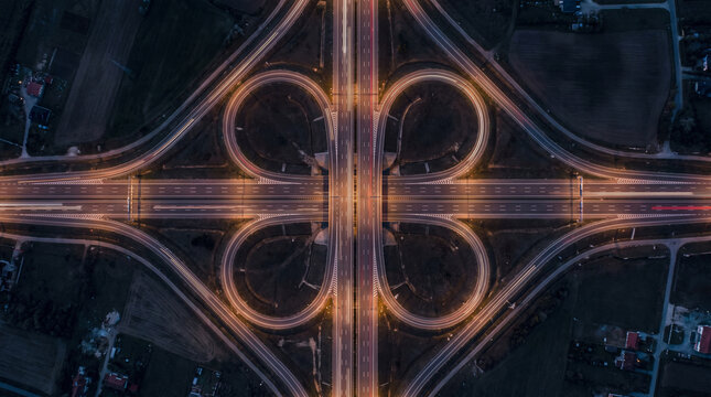 Aerial view of cloverleaf highway interchange illuminated at night, showing intricate road patterns and light trails.