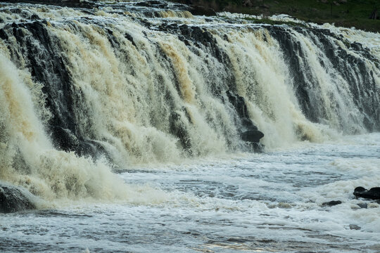 Powerful waterfall plunges over rugged rock formations, its sediment-tinted cascades creating dense spray and turbulent whitewater across rocky river below, Hopkins Falls, Cudgee, Victoria, Australia