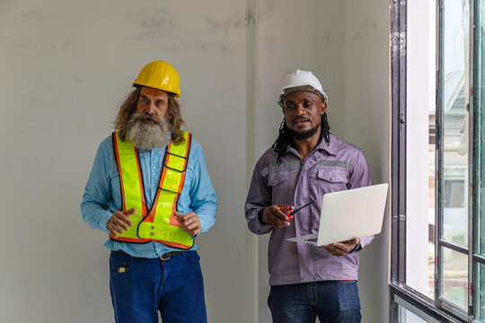 Two construction workers from different generations using a laptop to review progress together, highlighting teamwork, shared experience, and learning in a contruction place