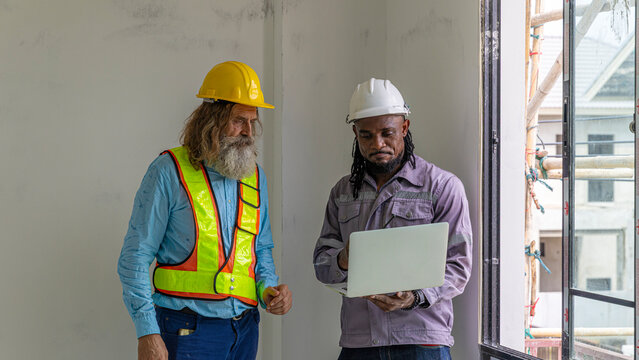 Two construction workers from different generations using a laptop to review progress together, highlighting teamwork, shared experience, and learning in a contruction place