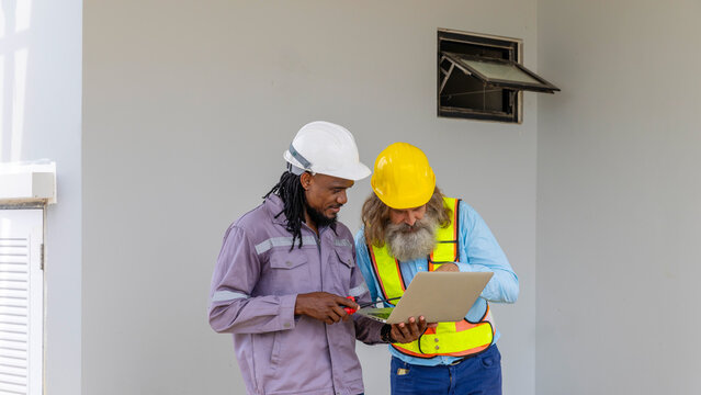 Two construction workers from different generations using a laptop to review progress together, highlighting teamwork, shared experience, and learning in a contruction place