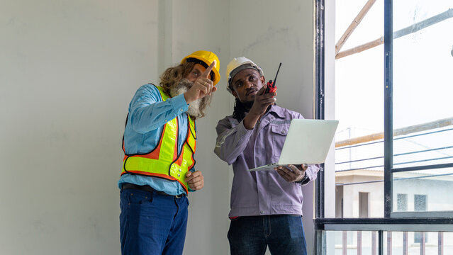 Two construction workers from different generations using a laptop to review progress together, highlighting teamwork, shared experience, and learning in a contruction place