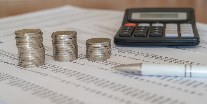 Stacks of euro coins descending across a financial statement with calculator and pen, symbolizing household budgeting, shrinking savings, rising expenses and cost of living pressures