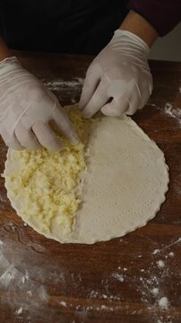 Chef adding cheese to traditional Arabic manakish flatbread on a floured wooden surface, preparing Middle Eastern cheese manakish in a restaurant kitchen.