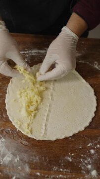 Chef adding cheese to traditional Arabic manakish flatbread on a floured wooden surface, preparing Middle Eastern cheese manakish in a restaurant kitchen.