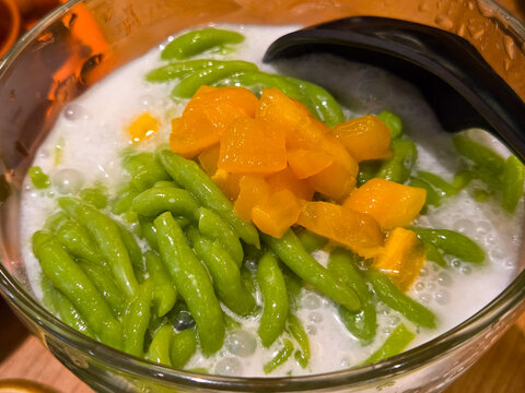Indonesian ice dessert Es Cendol with green rice flour jelly and sweet jackfruit topping in a transparent glass bowl