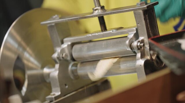 Close up of dried squid being pressed and shredded through a metal roller machine at street market.