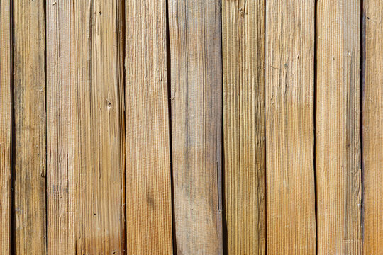 Natural wooden background made of vertical weathered planks with visible grain and rough texture, rustic timber surface with warm brown tones and narrow gaps between boards.