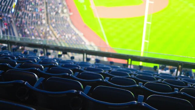 High angle view from empty stadium seats overlooking a professional baseball game, showing the diamond, green grass field, and blurred spectators watching the match