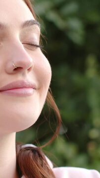 Vertical video: Sunlight drawing woman in pink top closing eyes smiling in garden nose ring visible