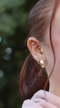Vertical video: Panning camera showing ear and jewelry of woman in light pink hoodie in park