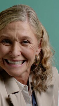 Vertical video: Smiling woman laughing as camera pulling back in studio, with gold hoops and blazer