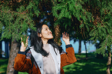 Outdoor scene with a smiling woman beneath hanging branches, arms raised, enjoying sunlight in a lush park, conveying happiness and nature connection for lifestyle and wellness themes © SHOTPRIME STUDIO