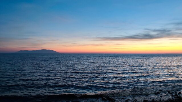 Photo of a beautiful sunset over the Thracian Sea in Alexandroupoli, Greece, featuring gentle water ripples, a colorful twilight sky, and the distant silhouette of Samothrace island on the horizon.