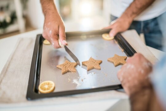 Gingerbread star cookies on a dark baking sheet being arranged by a man's hands, rustic homemade textures with copy space for a Christmas menu