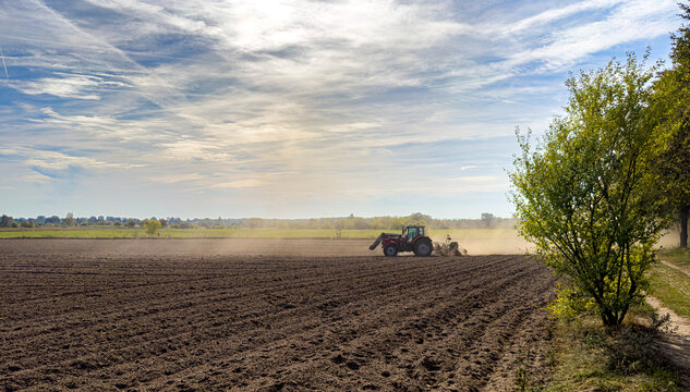 Roter Traktor bei der Aussaat auf einem staubigen Acker in weiter Landschaft unter bew&ouml;lktem Himmel, Berlin, Deutschland