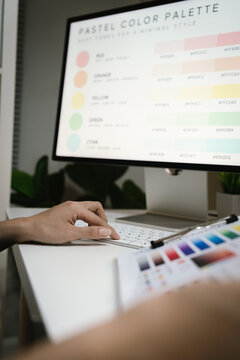 Interior designer selecting color palettes and reviewing home design concepts at a computer workstation, with a miniature house model and digital tablet on the desk.
