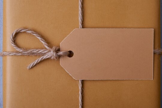 Blank gift tag tied with jute twine on a kraft paper parcel, featuring a fibrous texture and copy space for a mockup template