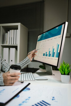 Business professional analyzing financial charts and sales performance on a computer monitor while reviewing reports at a modern office desk.