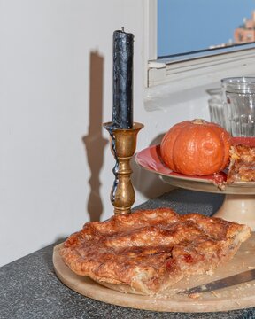 A partially eaten pie on a marble board with a black candle and pumpkin, featuring crumbly pastry and melted wax for after-party cleanup editorials