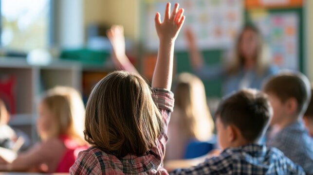 Child raising hand eager to answer question during classroom lesson with other students sitting and learning at desks
