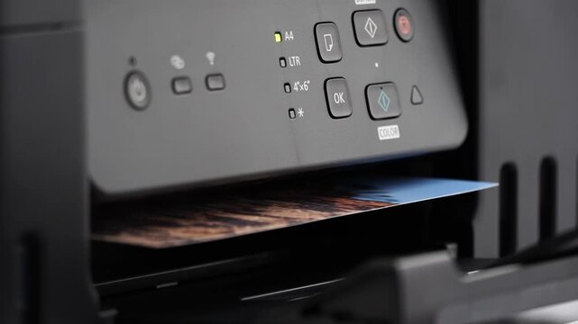 Printer ejects vibrant video from output tray. Control panel glows softly with operational lights. User-friendly interface features clear, modern buttons. Ideal for tech tutorials, home office scenes