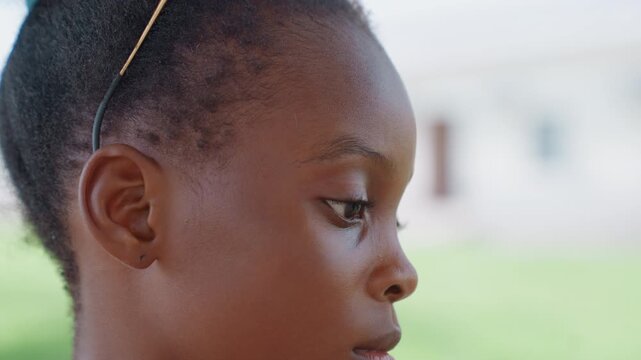 Close up portrait captures side profile of child face with braided hair and ear piercing set against soft outdoor background closeup girl view braids lighting
