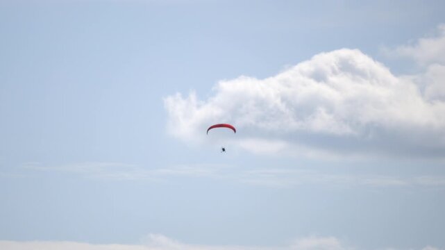 Parachutist soars above fluffy white clouds. Sky remains calm and blue with soft light. Red canopy glides gently through air. , just freedom in flight. Ideal for adventure, travel