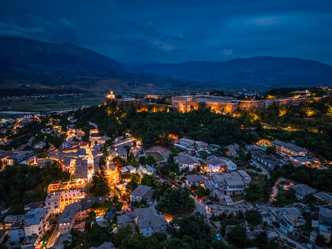 Illuminated Gjirokaster Castle overlooking the town at dusk with mountains in the background.