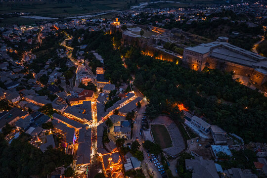 Illuminated Gjirokaster Castle overlooking the town at dusk with mountains in the background.