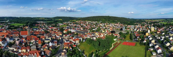 Malerische Luftaufnahme von Auerbach in der Oberpfalz mit der markanten Stadtpfarrkirche, traditionellen roten Dächern und idyllisch grüner Landschaft im Hintergrund unter blauem Himmel. © fotoping