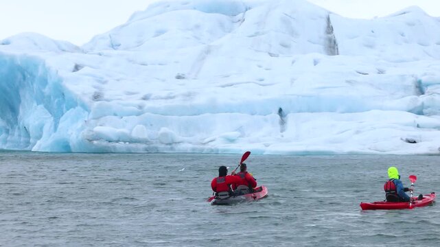 Three kayakers paddle together near a weathered iceberg in Svalbard