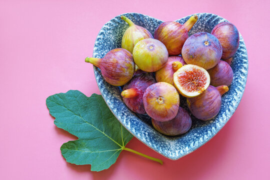 Ripe figs in heart-shaped plate on pink background. Flat lay, copy space