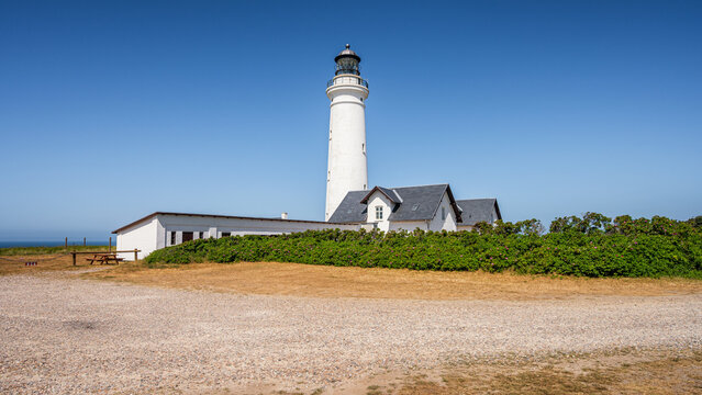 Scenic view of the historic white Hirtshals Fyr lighthouse and surrounding keeper houses in Denmark standing on a grassy field under a clear blue sky on a sunny summer day
