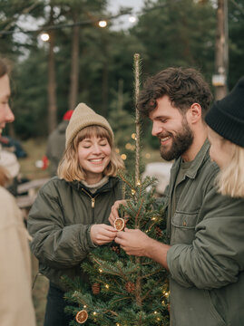 Young Couple Decorating Outdoor Christmas Tree with Dried Orange Slices