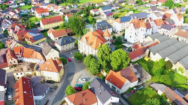 Malerische Luftaufnahme von Auerbach in der Oberpfalz mit der markanten Stadtpfarrkirche, traditionellen roten D&auml;chern und idyllisch gr&uuml;ner Landschaft im Hintergrund unter blauem Himmel.