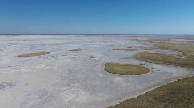 Camera panning right to left over the edge of the Makgadikgadi Salt Pans, Botswana, and the saltpans stretching to the horizon, 4K Aerial Video.