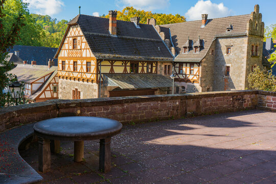 Historic half-timbered buildings and stone walls surrounding terrace at Schloss Ramholz, with autumn foliage under blue sky.