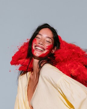 Indian woman with vibrant red powder on her face and hair, smiling joyfully in a bright high-key setting for cultural and festive themes