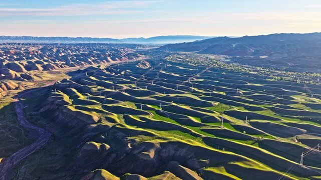 Aerial view of high-voltage transmission towers and power lines crossing rolling green hills in Xinjiang, China.