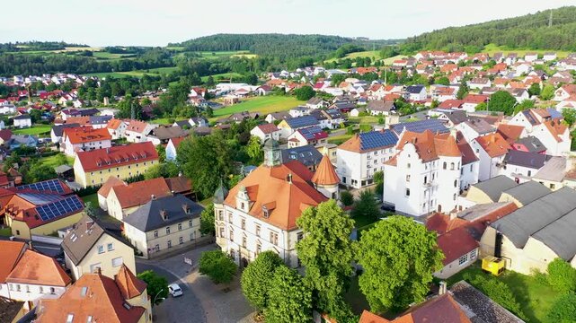 Malerische Luftaufnahme von Auerbach in der Oberpfalz mit der markanten Stadtpfarrkirche, traditionellen roten D&auml;chern und idyllisch gr&uuml;ner Landschaft im Hintergrund unter blauem Himmel.
